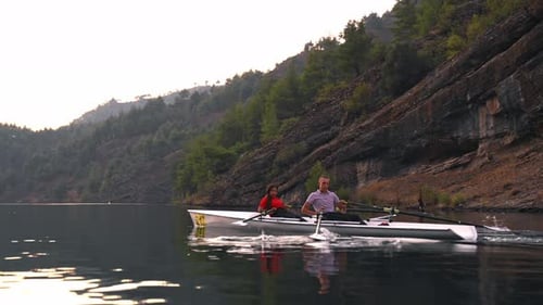 Rowing Boat on Calm Lake Near Rocky Hillside
