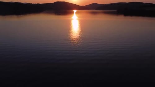 Cinematic aerial shot of stunning orange sunset above lake water