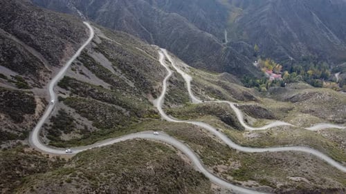 Aerial view: Vehicles ascend gravel road switchbacks up mountain slope