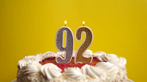 92. A candle in the form of the number 92, stuck in a holiday cake, is blown out. Celebrating a birt