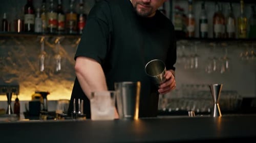 Un barman masculin tient une bouteille et verse magistralement la boisson dans un doseur en acier