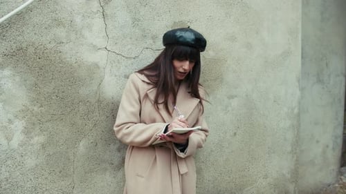 Stylish Woman Writes in Notebook Against Old Wall