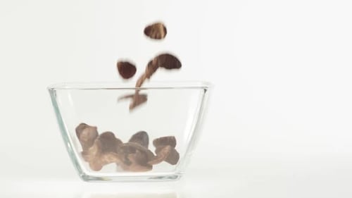 Chocolate cereal flakes fall in a transparent square bowl on a white background. Clean eating, detox