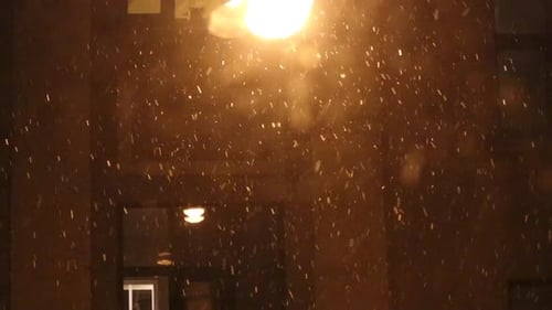 Peaceful view through window of snow falling on a cold dark December night with orange light in the