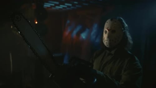 Man in the White Scary Mask Standing in the Warehouse and Posing with a Chainsaw Looking at the