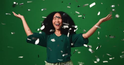 Happy woman, celebration and winning with jump in confetti for prize on a green studio background