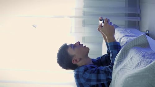 Young Adult Plays Video Game on Bed