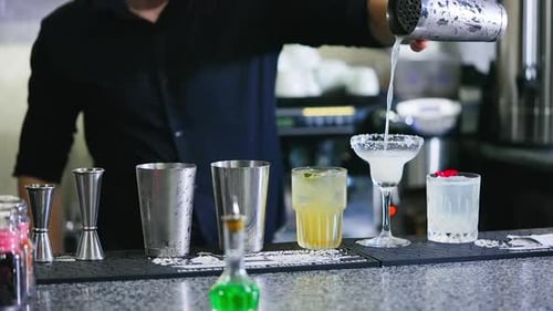 Barman in black shirt filling the wineglass with beverage. Glasses for cocktails making at the bar