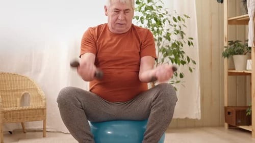 Hombre mayor maduro sentado en una pelota de fitness haciendo ejercicios de gimnasia con mancuernas, ejercicio deportivo