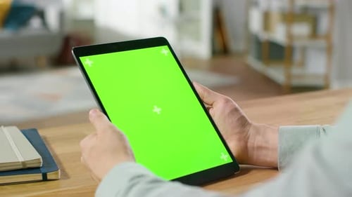 Man Using Green Mock-up Screen Digital Tablet Computer in Portrait Mode while Sitting at His Desk.