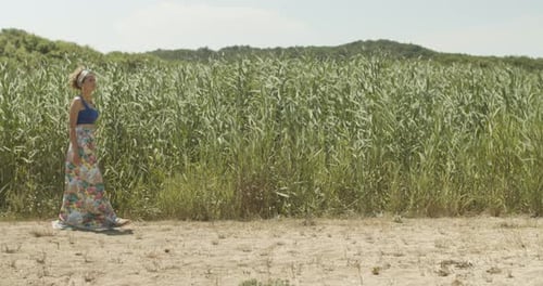 Pretty woman in summer skirt walks leisurely over beach, swaying reed background