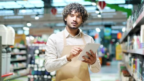 Portrait young staff man salesman in apron looking at camera in grocery store supermarket. Handsome
