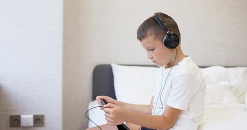 Child Wearing Headphones Using Smartphone on Bed