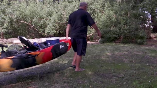 Pescador que lleva un kayak para pescar. El kayak tiene ruedas.