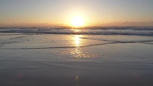 Golden hour ocean waves gently lapping on a sandy beach at sunrise.