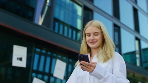 Young Woman Smiling While Texting on Smartphone Outdoors in Modern City