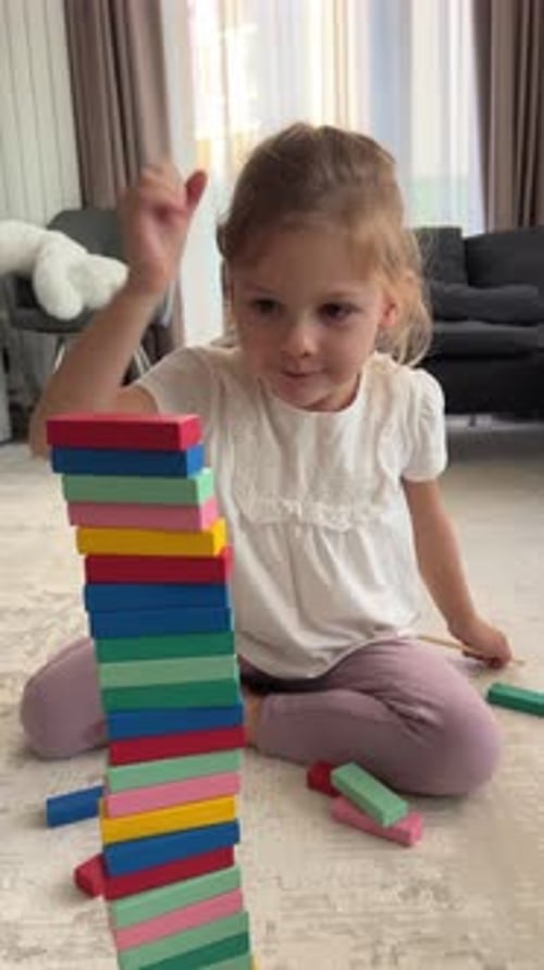 Vídeo vertical de una niña jugando a un juego de mesa en casa tomando bloques de colores de una torre de madera