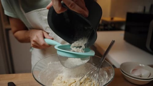 Person Sifting More Flour into the Batter, Adding Ingredients Gradually to Ensure Proper Mixing.
