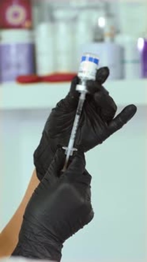 Mediziner, der Injektionsflüssigkeit aus der Ampulle in die dünne Spritze zieht, vertikale Ausrichtung