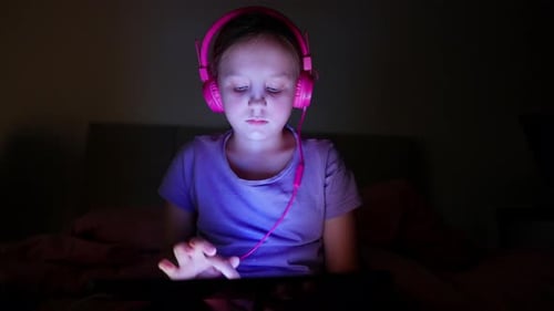 Child Uses Tablet with Headphones in Bed at Night