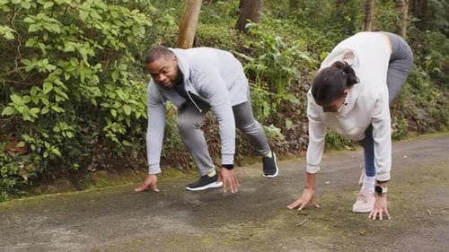 Diverse training duo crouching at sprint start on path wearing running shoes sprinting for speed