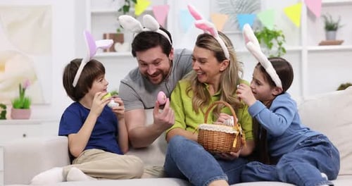 Easter celebration. Happy family with bunny ears and painted eggs on sofa at home