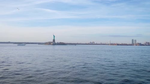 Wide shot of the Statue of Liberty in New York City from the river with a tour boat and birds in the