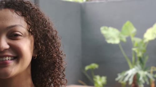 African American woman reacting to audio cue, smiling, laughing on patio near plants, copy space
