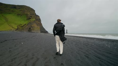 A Young Man Enjoying a Leisurely Stroll at Reynisfjara Black Sand Beach in Iceland