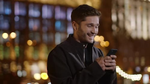 Happy Young Man Using Mobile Phone in City at Night