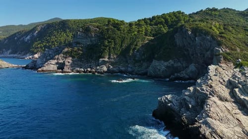 Rocky coastline with lush green hills and deep blue sea under a clear sky, aerial view