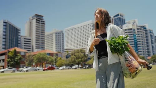 Mujer caminando por el parque de la ciudad con una bolsa reutilizable llena de productos frescos
