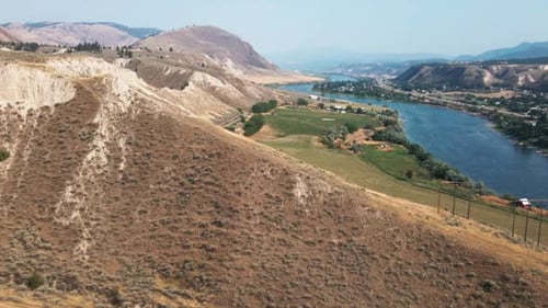 Beautiful aerial view of green field and lake with mountains and cloudy sky as background. Peaceful