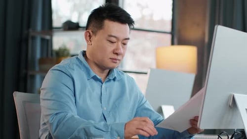 Focused Man Working at Desk With Documents and Computer in Modern Office Setting