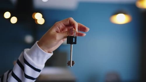Close Up of Female Hand Showing New House or Apartment Key to Camera on Modern Interior with Lights