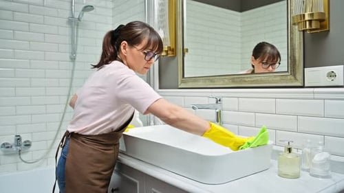Woman Cleaning Bathroom Sink with Yellow Gloves