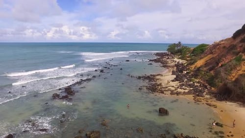 Touristes profitant des eaux chaudes d'une plage tropicale entourée d'une falaise abrupte et d'une côte magnifique