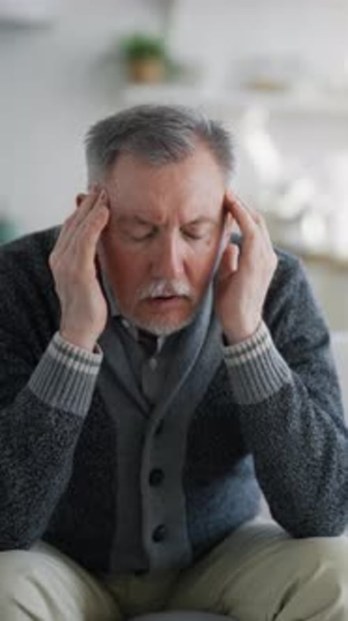 Senior Man Feeling Headache Massaging Temples Sitting on Sofa in Living Room Vertical Video Migraine