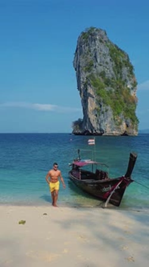 Young Men Walking on the Beach of Koh Poda Thailand with a Longtail Boat in the Ocean