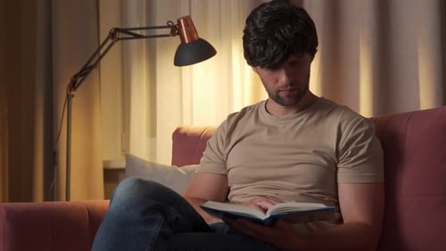 Adult Man Reading a Book on Sofa at Home