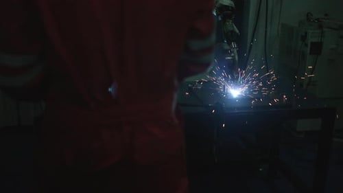 Blue collar workers at workshop with welding robot arm for automotive industry.