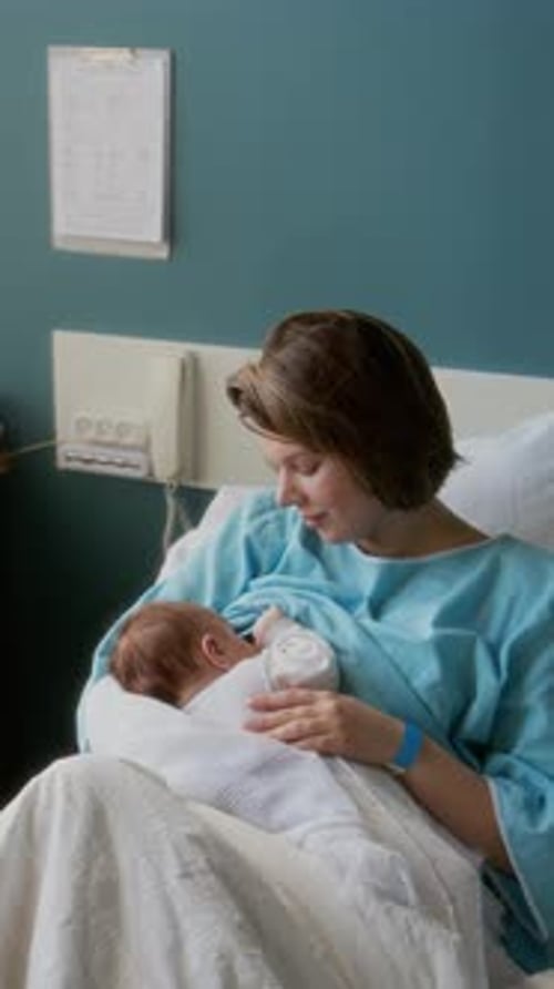 Mother Breastfeeding Newborn Baby in Hospital Bed