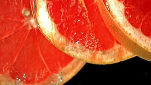 Grapefruit Slices Falling Into Water on Black Background