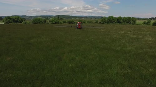 Der Traktor sprüht Grassamen über üppiges grünes Ackerland in einer wunderschönen ländlichen Landschaft