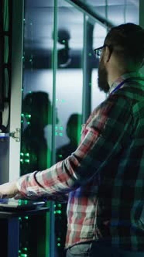 Man Working on Laptop in Dark Server Room