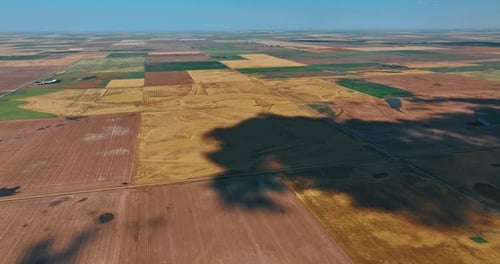 Big shadow from cloud spreads by the ground. Vast territory divided into the fields for agriculture.