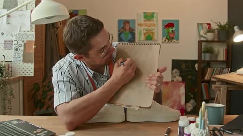 Artist Drawing in Sketchpad at Desk