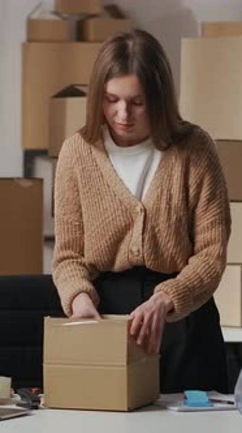 Young Woman Preparing Cardboard Packages at Desk Carefully Packing and Inspecting Cosmetic Products