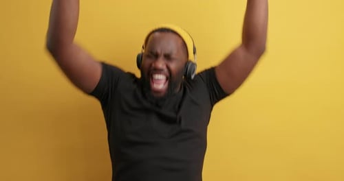 Upbeat dark skinned guy dances energetically shaking arms over yellow background