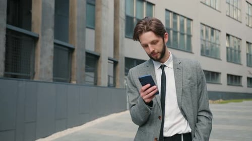 Young Employee Scrolling Phone Checking Social Media Man Looking in Camera Smiling Male with Beard